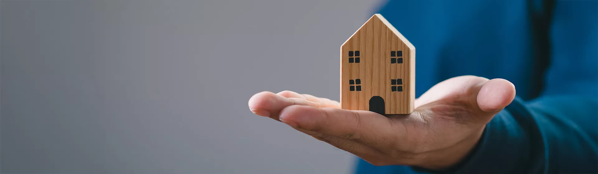 Nahaufnaheme eines Miniatur Holzhauses in einer männlichen Hand